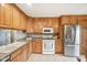 Well-lit kitchen featuring stainless steel refrigerator, white appliances, and wood cabinets at 3020 E 400 S, Lebanon, IN 46052