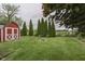 Spacious backyard with a fire pit, a red shed, and neatly trimmed evergreen trees, ideal for outdoor enjoyment at 454 E Broadway St, Greenwood, IN 46143