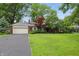 Charming brick home featuring an attached two-car garage, lush green lawn, mature trees, and professionally landscaped garden at 8752 Washington Blvd E Dr, Indianapolis, IN 46240