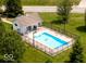 Aerial view of a backyard pool with a pool house and black fence, surrounded by well-maintained green grass and mature trees at 425 Bridgewater S Ln, Muncie, IN 47304