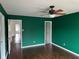 A bedroom features wood floors, bold green walls, a ceiling fan, and multiple doors at 4456 Redcliff N Ln, Plainfield, IN 46168