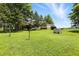Expansive backyard with lush green grass, mature trees, and outbuildings under a clear blue sky at 25420 Jerkwater Rd, Sheridan, IN 46069
