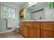 Bright bathroom with light green walls, wooden cabinets, and a window offering outdoor views at 4013 Hillendale Dr, Greenwood, IN 46142