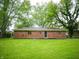 Brick home back view highlighting a vast lawn and a shady tree backdrop at 21 Roderick Ct, Beech Grove, IN 46107