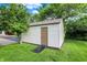 Image of a vinyl sided shed with a ramp and a solid door nestled in a green lawn with surrounding trees at 4495 W Stones Crossing Rd, Greenwood, IN 46143