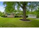 Charming home exterior featuring a red front door, large tree and green lawn at 7482 W Us Highway 40, Indianapolis, IN 46229