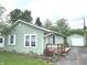 Charming single-story home features a light green exterior, wooden deck, and a detached garage, offering a cozy and inviting curb appeal at 1801 Bauer Rd, Indianapolis, IN 46218