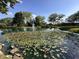 Scenic pond with lily pads, a central fountain, and mature trees under a clear sky at 7601 Newport Bay Dr # 203, Indianapolis, IN 46240
