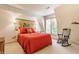 Sunlit bedroom with neutral carpet, red bedding and a charming rocking chair at 5326 White Marsh Ln, Indianapolis, IN 46226