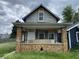 Exterior shot of a dilapidated home with a brick porch, boarded windows, and overgrown lawn at 243 Iowa St, Indianapolis, IN 46225
