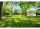 Expansive lush green yard, partially shaded by mature trees with outbuildings and trampoline at 5253 W 8Th Street Rd, Anderson, IN 46011