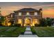 Charming two-story brick home with manicured lawn, elegant entrance, and warm exterior lighting at sunset at 6639 E Deerfield Dr, Zionsville, IN 46077