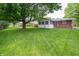 This back yard features lush grass, landscaping, mature trees, and a partial view of the house at 5903 Schoolwood Dr, Speedway, IN 46224
