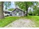 View of cozy home with gray siding, green door, mature trees, and gravel driveway at 1841 New St, Indianapolis, IN 46203