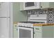 A close up of the updated white oven, light green cabinetry, and decorative backsplash at 2645 Washington St, Columbus, IN 47201