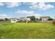 Large backyard featuring green grass, a wooden fence, playset, and houses in the distance under a blue sky at 4434 W Windsong Ct, New Palestine, IN 46163