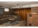 Cozy basement living area offers a comfortable sofa, brick fireplace, and rustic wood paneling at 3431 W Mooresville Rd, Indianapolis, IN 46221