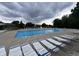 Bright blue community pool with rows of lounge chairs, a lifeguard stand, and a sun shade against a backdrop of trees and cloudy skies at 1287 Highland Lake Way, Brownsburg, IN 46112