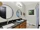 Bathroom featuring double sinks, black granite countertops, wooden cabinetry, and dual round mirrors at 4123 S Village Row, New Palestine, IN 46163