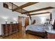 Bedroom with exposed beams, wood floors, a large bed and matching dresser with access to a loft and ensuite bathroom at 4623 E Windsor Ln, Columbus, IN 47201