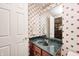 Powder room featuring a dark marble countertop, wood vanity, and patterned wallpaper at 5404 Cayman Dr, Carmel, IN 46033