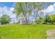 The home sits on a spacious, grassy lot under a blue sky, with mature trees and street access at 564 S Bosart Ave, Indianapolis, IN 46203