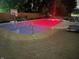 Backyard pool lit in red at night, featuring a basketball hoop and lounge chairs on a brick patio at 7935 N County Road 650 E, Brownsburg, IN 46112