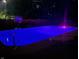 Backyard pool illuminated with purple light at night, framed by a fence, plants, and basketball hoop at 7935 N County Road 650 E, Brownsburg, IN 46112