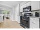 Well-lit kitchen with black appliances, white cabinetry, light countertops, and view to living room at 450 N Fenton Ave, Indianapolis, IN 46219