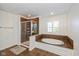 Bathroom with walk-in shower featuring glass door and soaking tub beneath window with shuttered blinds at 12772 Tram Ln, Carmel, IN 46032