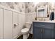 Elegant powder room featuring floral wallpaper, wainscoting, a blue vanity, and marble countertop at 14149 Ledgewood Way, Carmel, IN 46032