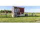 A charming red chicken coop stands elevated on a grassy lot enclosed by a fence at 3840 W 38Th St, Anderson, IN 46011