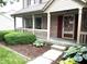 Inviting covered front porch with brick accents and a garden with blooming flowers at 10760 Independence Way, Carmel, IN 46032