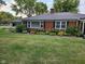 A classic brick ranch home showcases a modern metal roof and lush foundation landscaping at 1322 Greenway Dr, Anderson, IN 46011