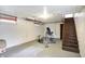 Unfinished basement with exercise equipment, concrete floor, and access to wooden staircase at 3940 E 57Th St, Indianapolis, IN 46220