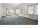 A spacious living room with multiple windows providing natural light, complemented by an elegant chandelier and green carpet at 6125 Winthrop Ave, Indianapolis, IN 46220