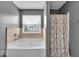 This bathroom features gray walls, a bathtub with stone surround, a shower with a patterned curtain, and a window at 2434 Burgundy Way, Plainfield, IN 46168