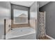 This bathroom features gray walls, a bathtub with stone surround, a shower with a patterned curtain, and a window at 2434 Burgundy Way, Plainfield, IN 46168