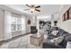 Well-lit living room with access to dining area and modern kitchen, featuring gray furniture, ceiling fan, and a large window at 2434 Burgundy Way, Plainfield, IN 46168