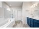 Bright bathroom featuring a large soaking tub, glass enclosed shower, and blue vanity with lots of storage at 8635 Verbena Rd, Zionsville, IN 46077