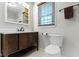 Bathroom featuring a wooden vanity, mirror with lighting, toilet, and a large window at 11461 N College Ave, Carmel, IN 46032