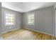Sunlit bedroom with gleaming hardwood floors and two windows overlooking a green outdoor space at 11461 N College Ave, Carmel, IN 46032
