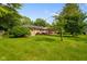 Large backyard featuring a brick home, lush lawn, mature trees, and wooden deck with an awning at 1506 Bowman Dr, Greenfield, IN 46140