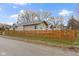 Tan home featuring a wood fence, well-maintained lawn, and tree line, all showcased under a bright, partly cloudy sky at 802 N Tuxedo St, Indianapolis, IN 46201