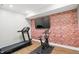 Home workout room featuring a treadmill, exercise bike, and accent brick wall with mounted TV at 16244 Perrault Ct, Fishers, IN 46040