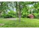 Large backyard showcasing a basketball court, storage shed, mature trees, and lush green grass at 3425 Ireland Dr, Indianapolis, IN 46235