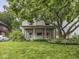 View of a two-story home with charming front porch, American flag, and mature tree shading the lawn at 4455 Central Ave, Indianapolis, IN 46205