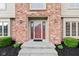 Close-up of a classic brick home's entryway with a red front door and manicured landscaping at 1826 Spruce Dr, Carmel, IN 46033