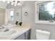 Bathroom with ceramic countertops, grey cabinetry, vanity mirror, updated fixtures, and window with a view of nature at 6644 Mcfarland Rd, Indianapolis, IN 46227