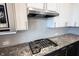 Close up of a modern gas cooktop, granite countertop, and stainless steel vent hood with white cabinets at 14982 Dawnhaven Dr, Westfield, IN 46074